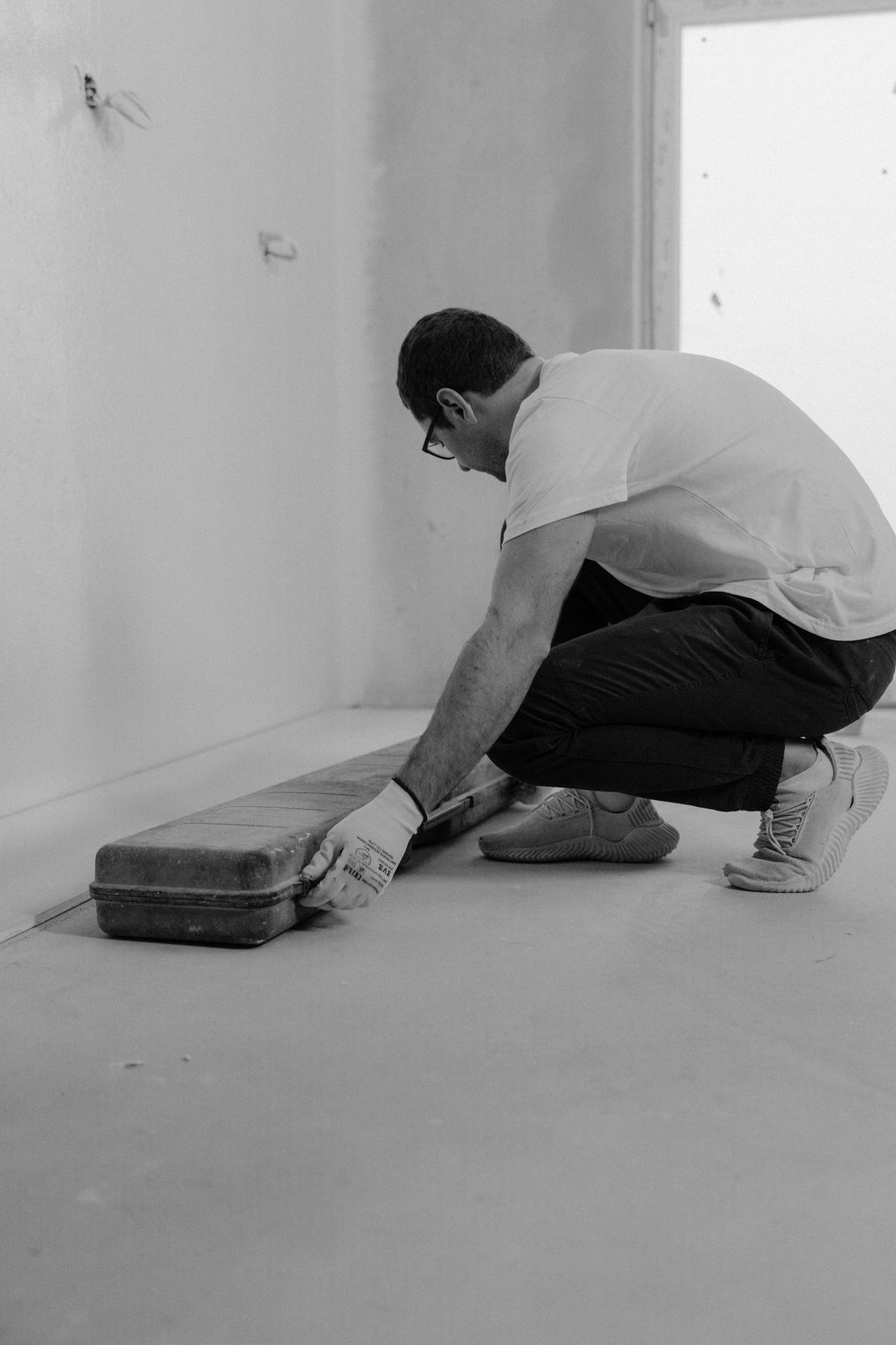 A tiler kneeling at floor level with a tool in hand, working across a prepared floor