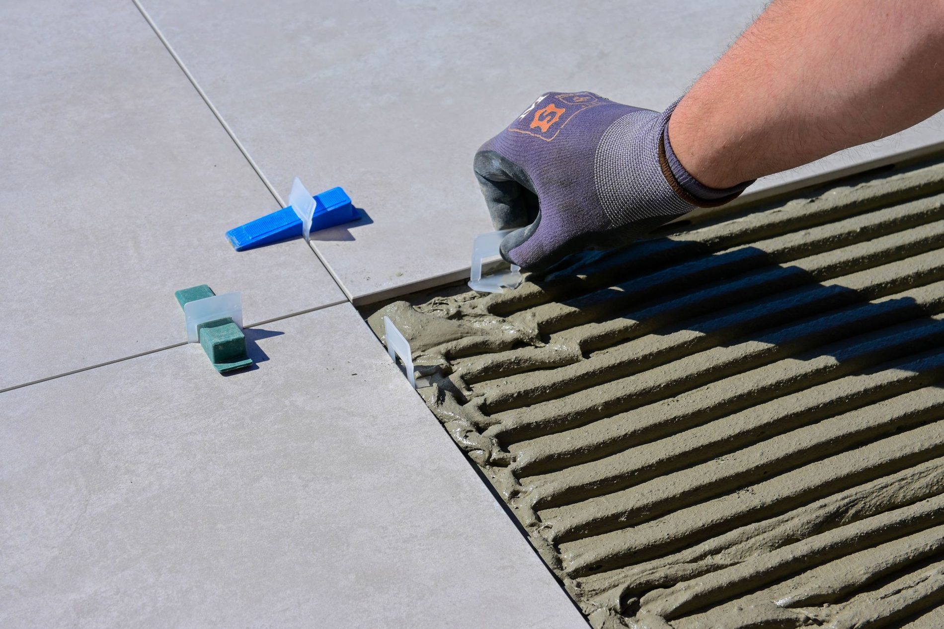A notched trowel combing tile adhesive across a floor in even ridges