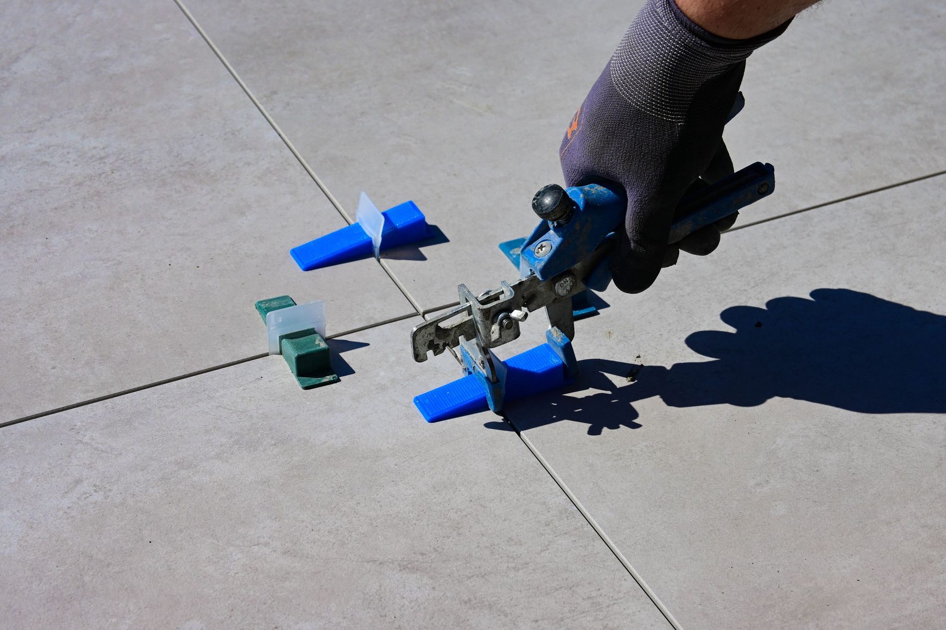A gloved hand fitting a tile levelling clip into the joint between two large floor tiles