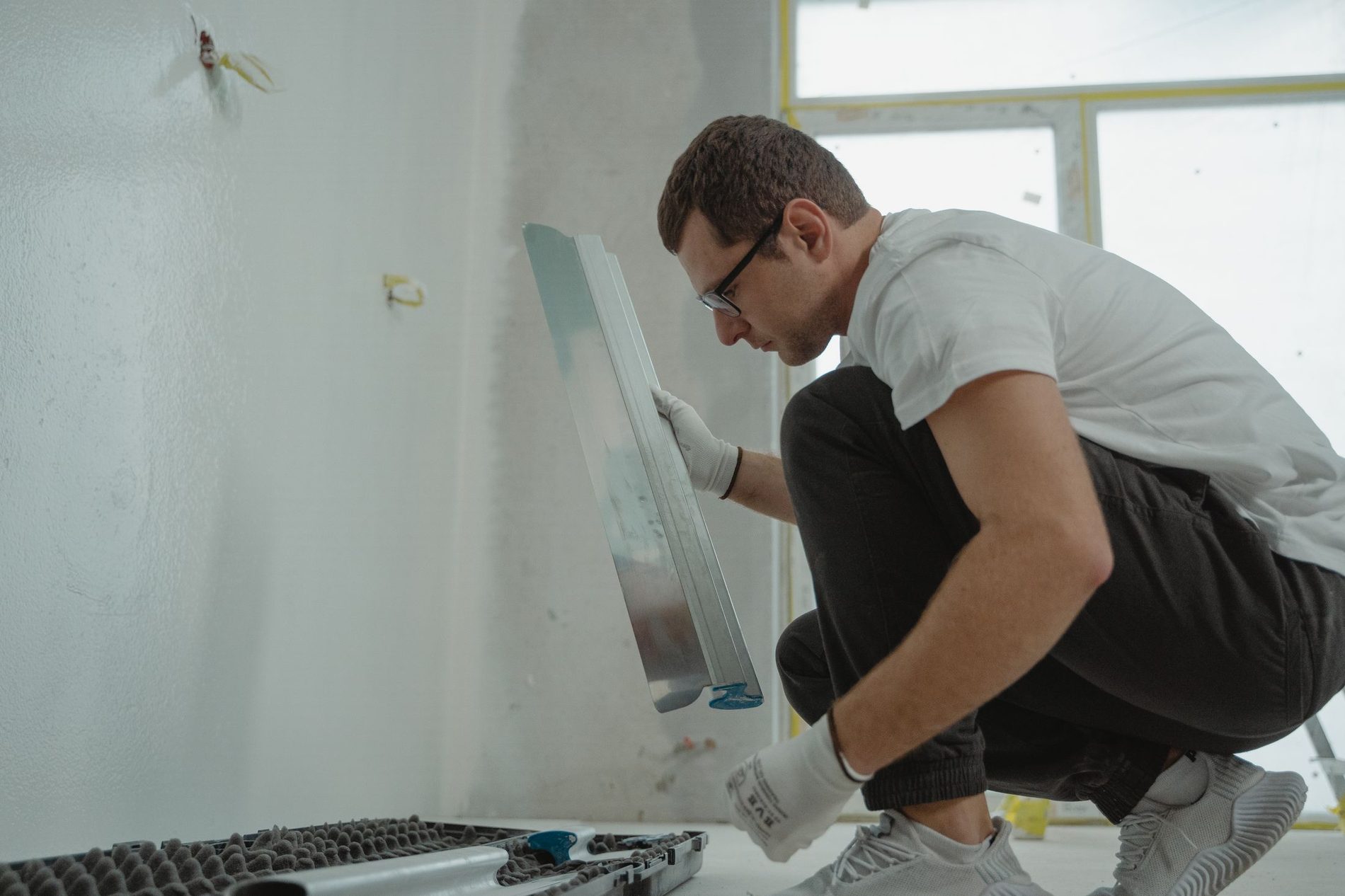 A tradesman preparing a bare wall in a stripped room before tiling begins